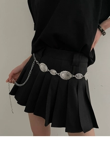 Détail de la ceinture chaîne en métal argenté vintage sur une jupe plissée noire