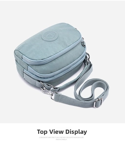 Detail view of light blue nylon crossbody bag with multi-layer zippers and logo