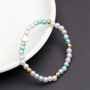 Close-up of pastel pearl beaded bracelet with heart charm on a white ceramic plate