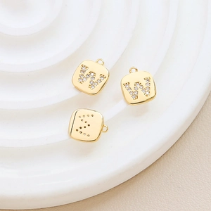 Macro detail of gold plated cubic zirconia alphabet pendants W and S on a ceramic tray