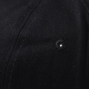 Macro shot of embroidered ventilation eyelet and twill cotton texture on a black baseball cap