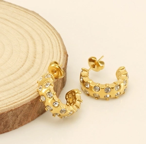 Close-up of gold-plated C-shape hoop earrings with white crystals on a wooden base