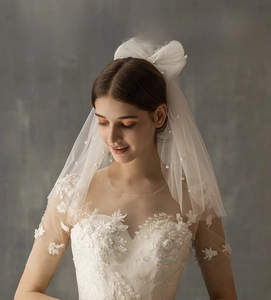 Detail of short double-layer white bridal veil with pearls, bow, and lace embroidery