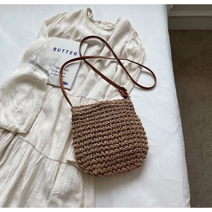 Flat lay of a brown woven straw crossbody bag styled with a white dress and props