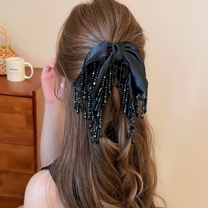 Détail de la pince à cheveux noeud en soie noire avec glands perlés sur cheveux bouclés