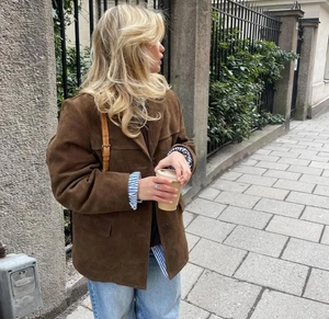 Brown faux suede jacket styled with a striped shirt in an urban outdoor setting