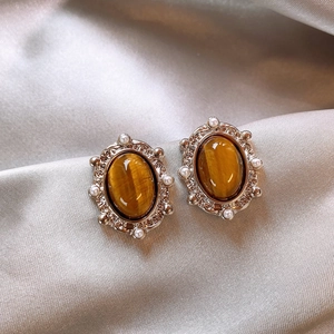 Detailed shot of gold tiger eye earrings with pearl embellishments on beige silk