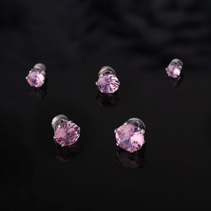 Macro detail of magnetic stud earrings with pink zircon stones on a black reflective base