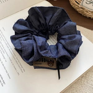 Close-up of dark blue denim hair scrunchie with teddy bear label on a vintage book