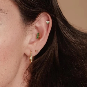 Detail of gold stud earrings with three asymmetrical green and white zircon stones