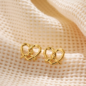 Macro shot of gold pretzel heart stud earrings on beige woven fabric background