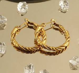 Close-up of golden twisted hoop earrings on a reflective mirror with ice cube accents
