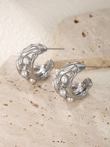 Detail of silver hollow earrings with lava texture and white pearls on beige stone