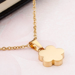 Polished gold flower pendant necklace with delicate chain on pink marble background