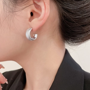 Macro shot of silver textured C-shaped hoop earrings worn by a model in a black suit