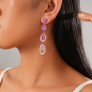 Macro detail of geometric long tassel earrings featuring pink rhinestone gradient