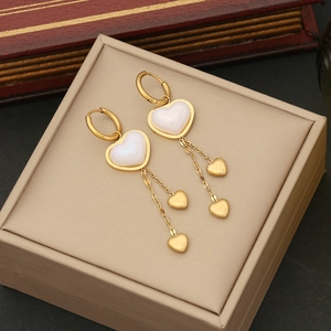 Elegant gold heart earrings with pearl tassel on a beige jewelry box with vintage book decor