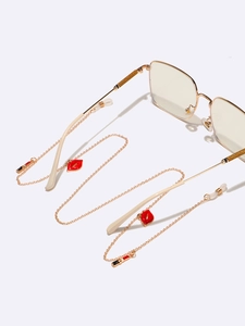 Detail of gold eyewear chain featuring red enamel lip and lipstick charms with silicone grips