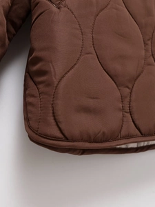 Macro detail of the dark brown quilted jacket showing the gourd stitching and fabric texture