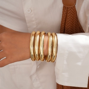 Close-up of five-piece minimalist gold geometric bangles worn with elegant white linen