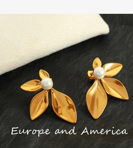 Macro shot of gold leaf earrings with round white pearl center on textured stone