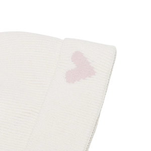 Close-up of a white ribbed knit beanie featuring a small pink heart detail on the cuff