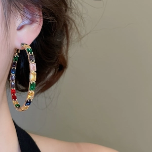 Close-up of a large gold hoop earring with colorful rectangular zircons worn by a model