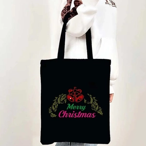 Black canvas tote bag featuring Merry Christmas bells print held by a model in white hoodie