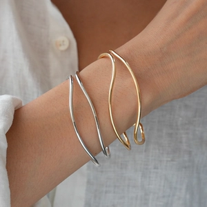 Minimalist gold and silver irregular wave layered open bangles worn on a wrist