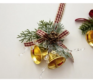 Close-up of golden metal bells with pine cones, greenery, and red plaid ribbon bow