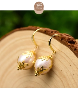 Detailed macro view of baroque pearl earrings with golden leaf design on wood background