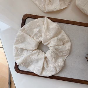 Detailed view of floral embroidery on a beige cotton scrunchie over a wooden frame
