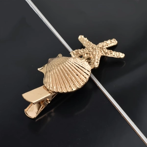 Detailed close-up of golden starfish and seashell hair clip with sleek metal texture