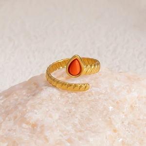 Detail of twisted 18k gold plated ring with teardrop orange stone on stone background