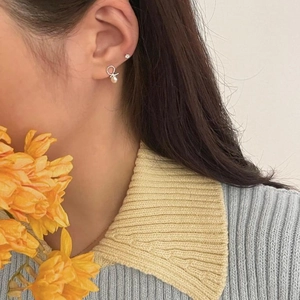 Close-up of elegant silver twist pearl stud earring worn by model with floral background