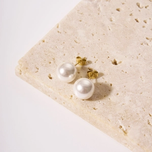 Boucles d'oreilles perles minimalistes dorées 18K sur un support en pierre beige