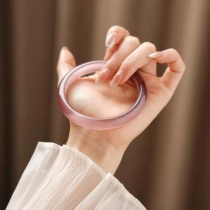 Close-up of translucent pink cat-eye stone bangle worn on wrist with soft lighting