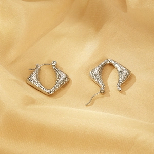 Close-up of silver geometric earrings with hammered texture on champagne satin fabric