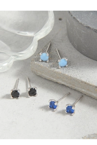 Detail of 925 sterling silver mini earrings with blue and black gemstones on a concrete surface