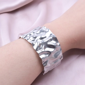 Detail of silver textured cuff bracelet with irregular wrinkled pattern on satin background