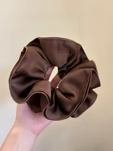 Close-up of a large dark brown silk scrunchie with soft satin texture and pleated edges