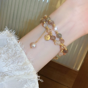 Detail of a layered beaded bracelet with gold coin charms and freshwater pearl on wrist
