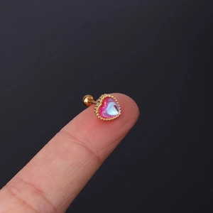 Macro detail of a heart-shaped moonstone ear stud with gold plating on a finger for scale