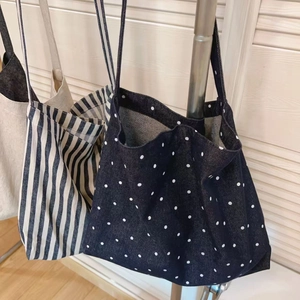 Three canvas tote bags in polka dots and stripes hanging on a metal rack display