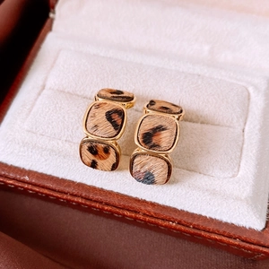 Detail view of gold-plated leopard print geometric hoop earrings on a cream jewelry box