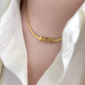 Detail shot of a golden MOM letter pendant on a sleek snake chain worn by a model