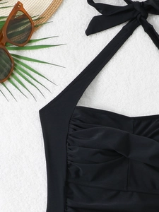 Detailed view of black halter neck swimsuit featuring elegant pleats and textures