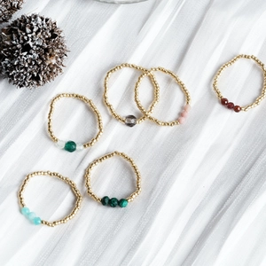 Set of 6 handmade golden beaded rings with colorful natural stone accents on white fabric