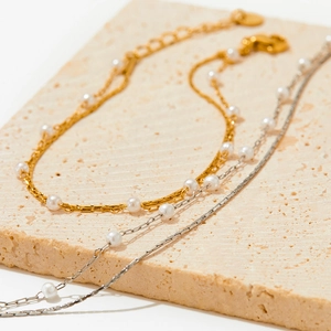 Layered gold and silver stainless steel pearl bracelets set on a beige stone base