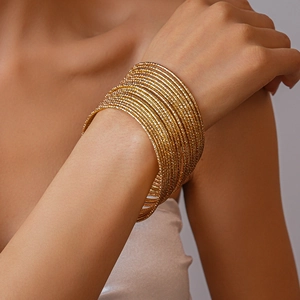 Dettaglio di 20 bracciali rigidi dorati sovrapposti con finitura testurizzata sul polso